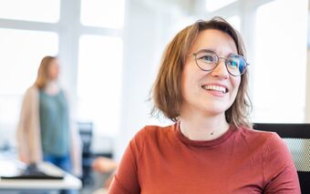 Annkatrin Göpfert sitzt im Büro der agorum Academy, im Hintergrund ist eine weitere Person zu sehen.
