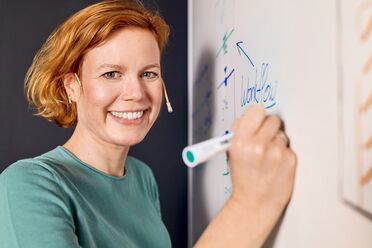 Indra Cloet schreibt den Begriff 'Workflow' auf ein Whiteboard im Rahmen des Projektmanagements.