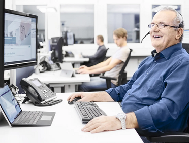 Ein Mitarbeiter sitzt am Schreibtisch und nutzt das Dokumentenmanagement-System, während Kollegen im Hintergrund arbeiten.