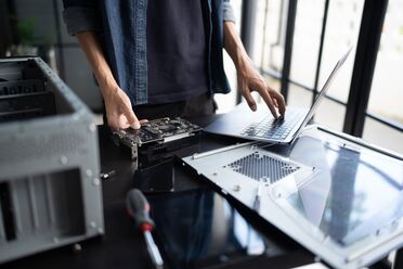 Eine Person zeigt eine GPU-Karte während sie an einem Laptop arbeitet, um den KI-Server von Thomas-Krenn.AG zu konfigurieren.