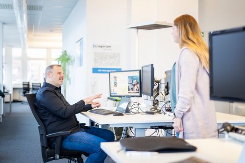 Ein Mitarbeiter demonstriert die Workflowentwicklung in einem modernen Büro mit mehreren Bildschirmen und einem Laptop.