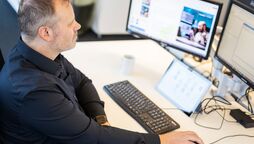 Ein Mitarbeiter arbeitet an einem Schreibtisch mit mehreren Monitoren, die das Dokumentenmanagement-System anzeigen.